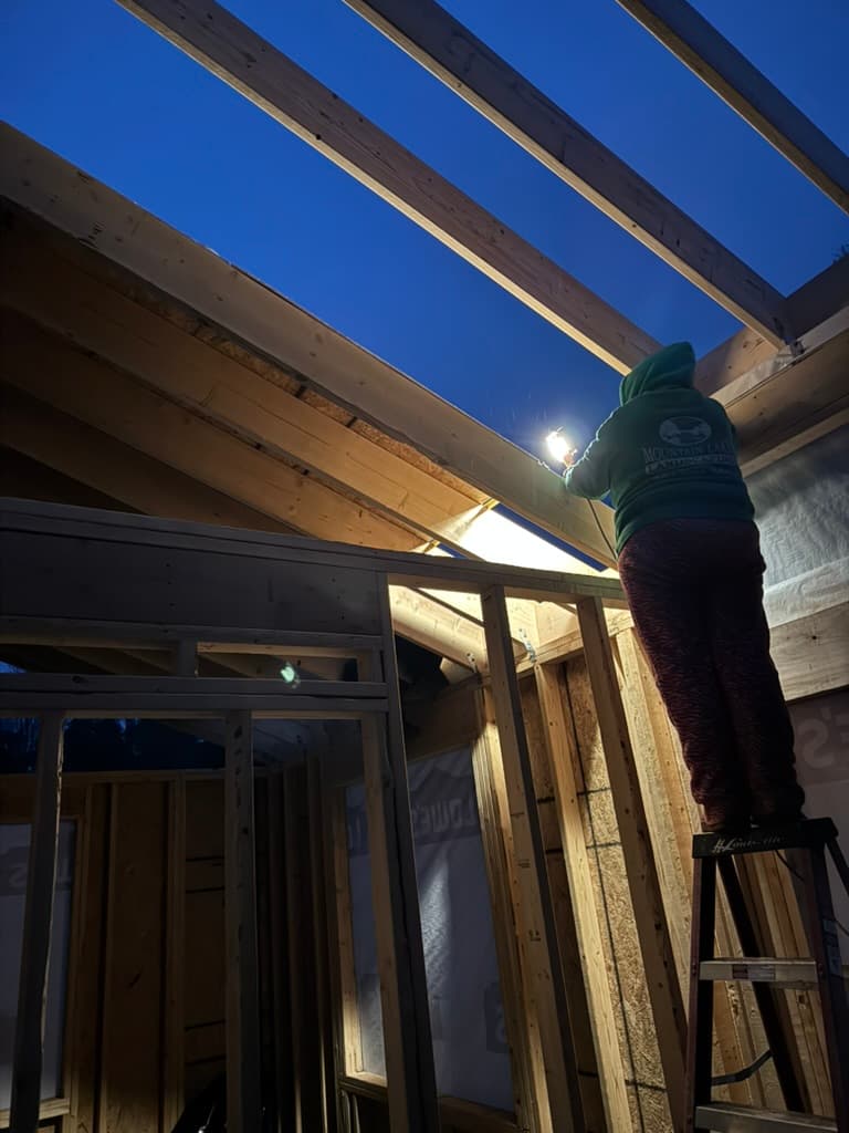 Real Elite crew member framing a custom addition by work light at dusk