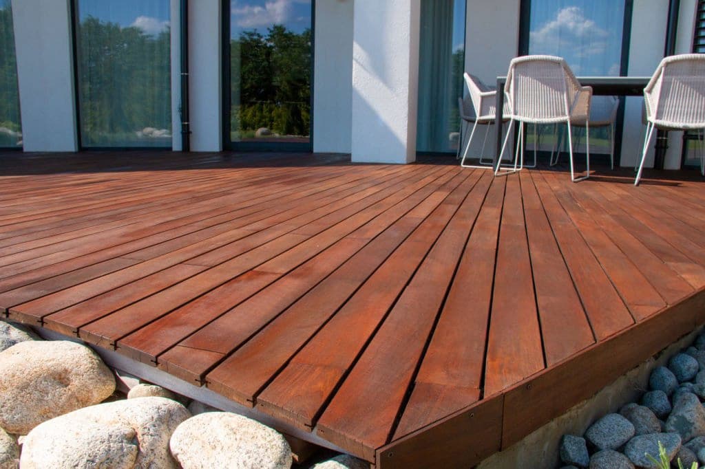 IPE hardwood deck wrapping a modern glass-walled home with white woven dining chairs
