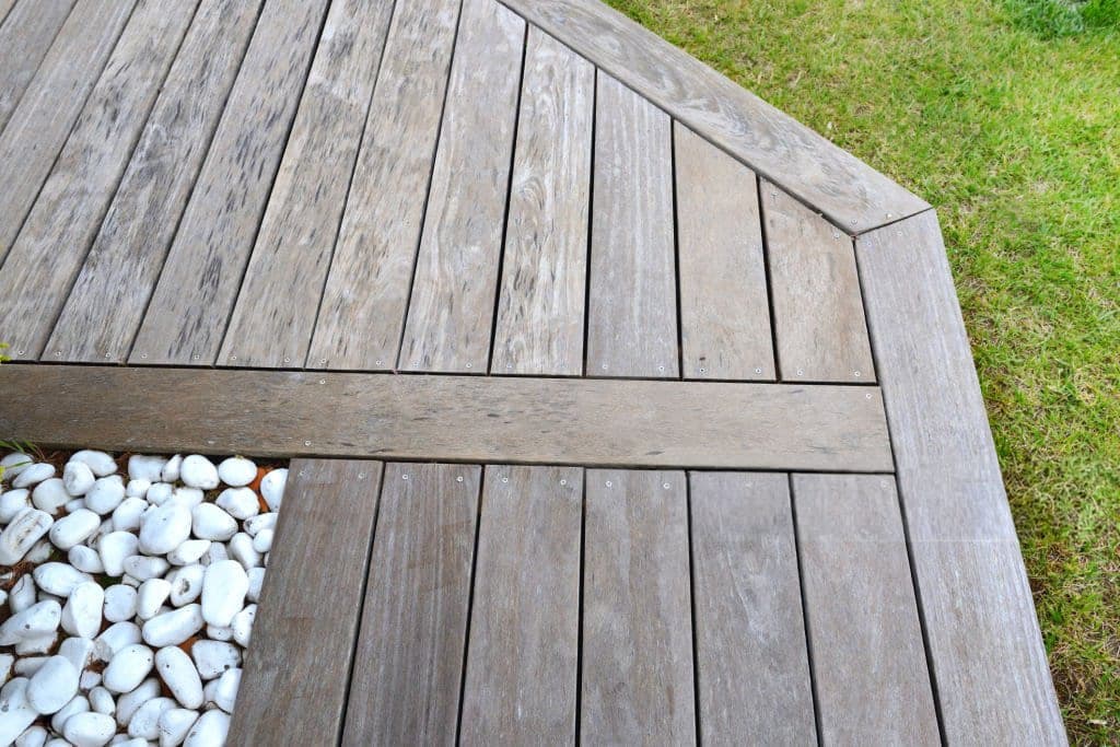 Weathered wood deck corner with white pebble accent inlay and grass edge