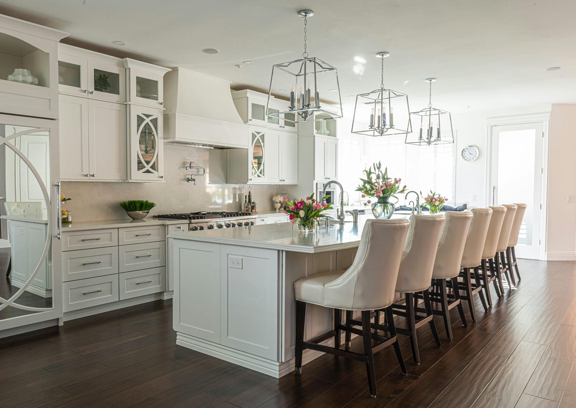 White kitchen with marble-topped island, lantern pendants, and dark hardwood floors