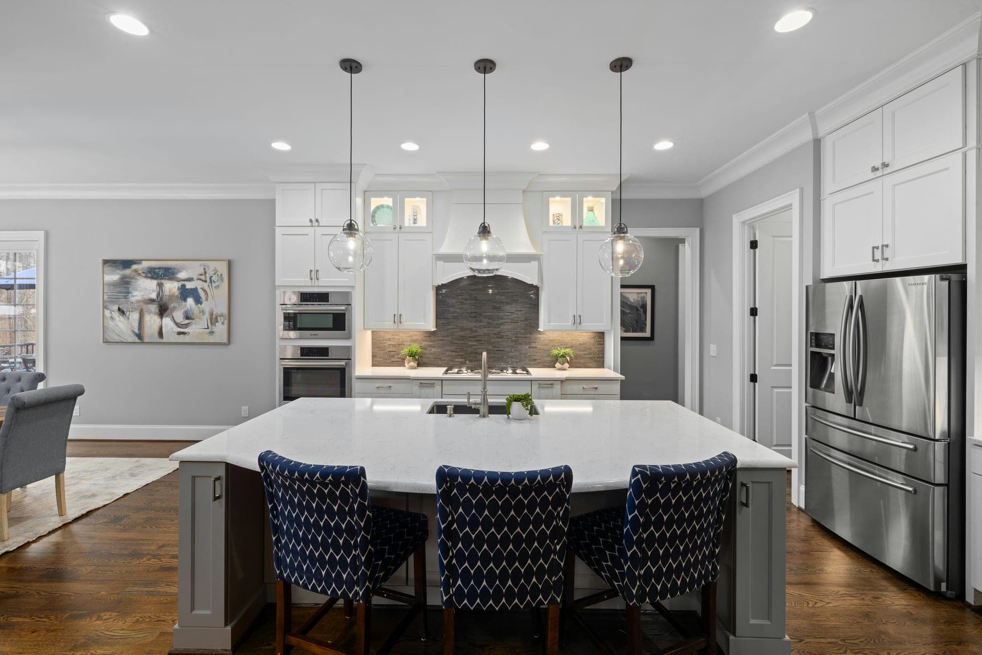 Open white kitchen with center island, navy chairs, and abstract artwork