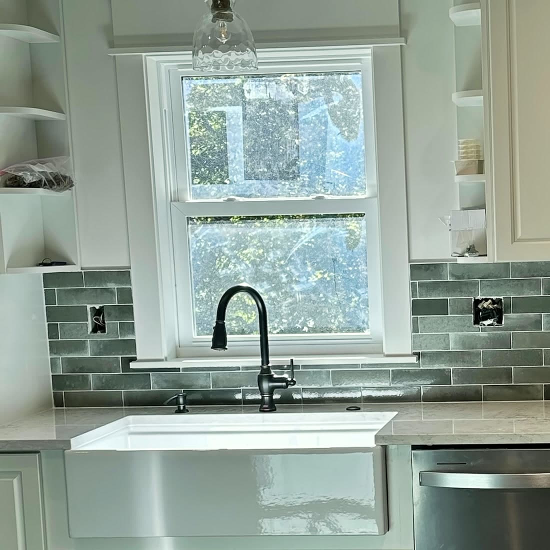 Gray glazed subway tile backsplash around a window above a white farmhouse sink