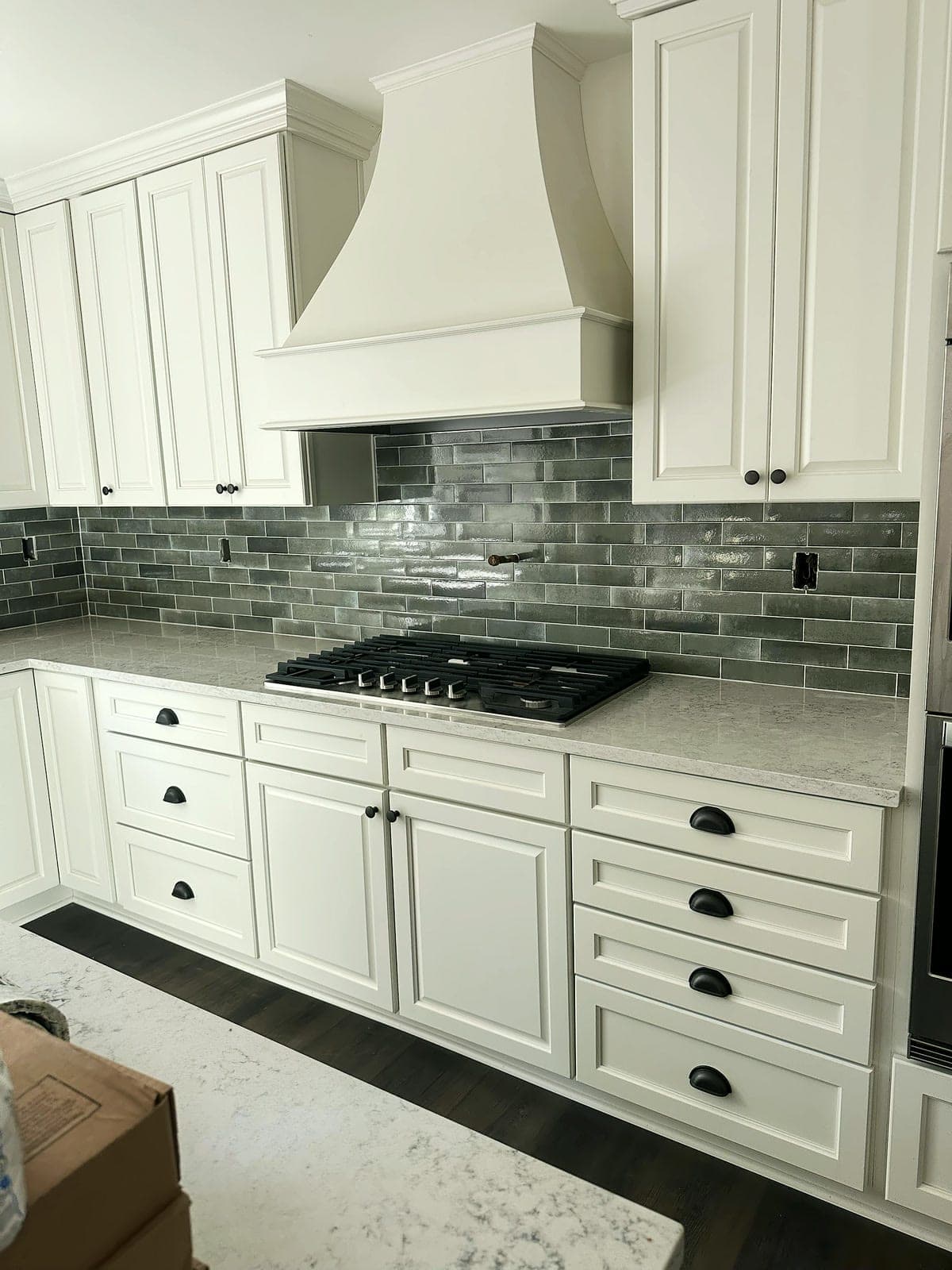Gray glazed subway tile backsplash behind a gas cooktop under a white range hood