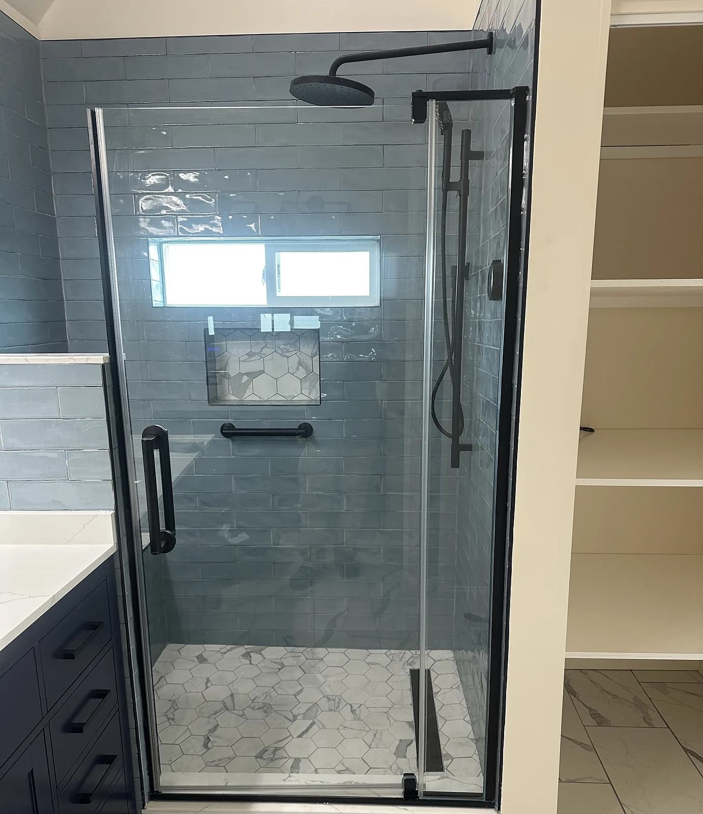 Walk-in shower with frameless glass, blue subway tile, marble-look hex floor, and matte black fixtures