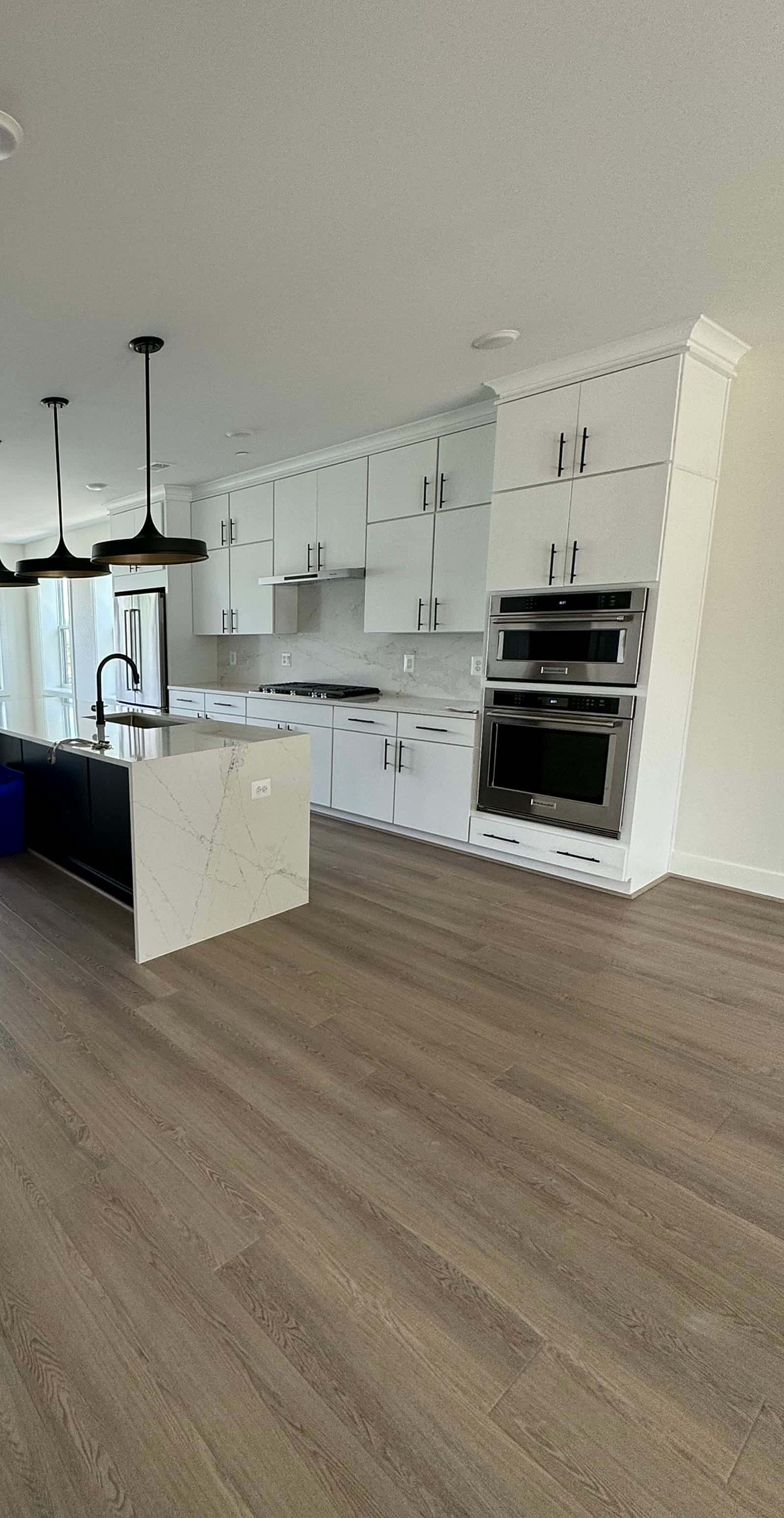 White shaker kitchen with a black waterfall-edge quartz island, black pendants, and double wall ovens