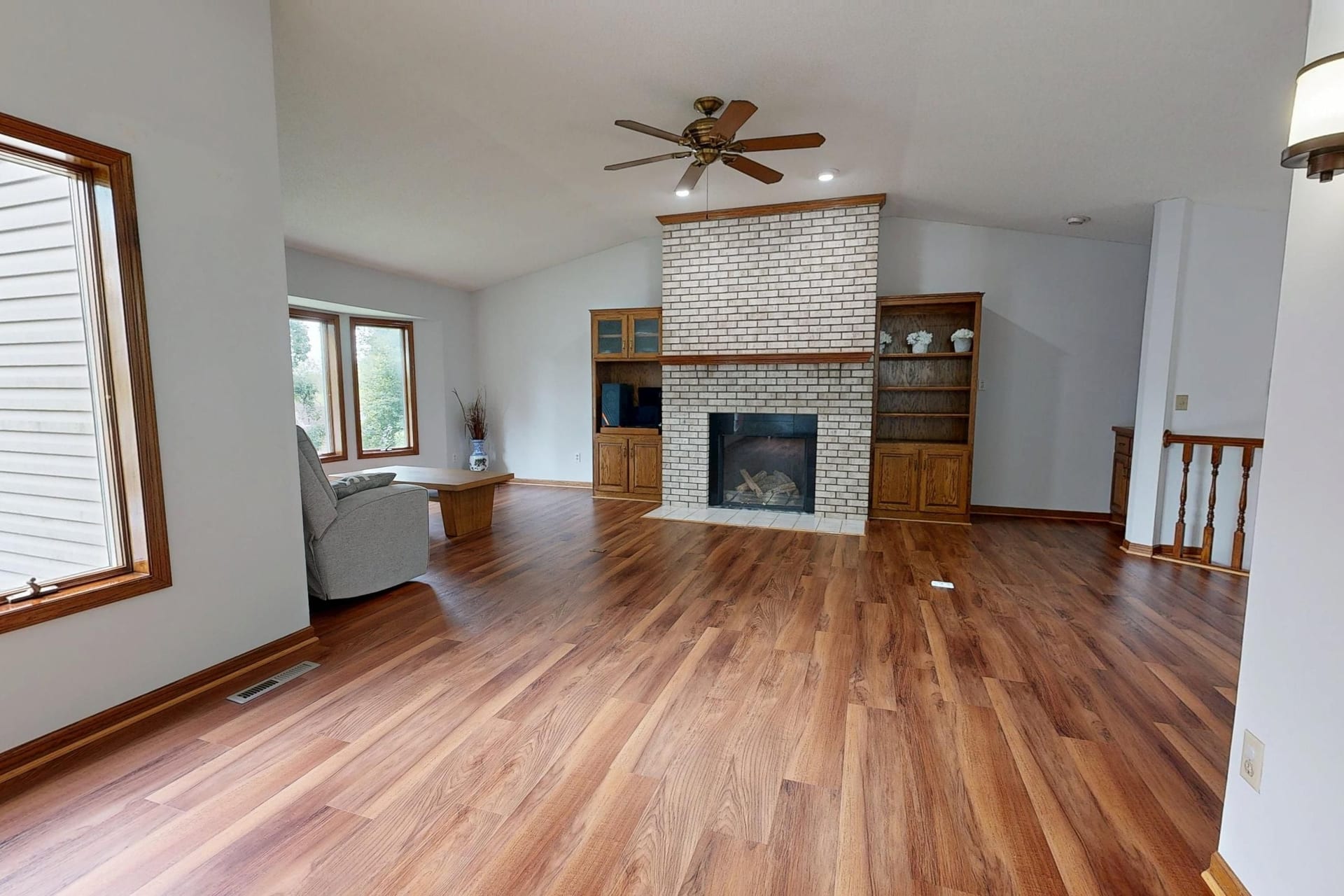 A bright living room with warm wide-plank hardwood flooring and a brick fireplace