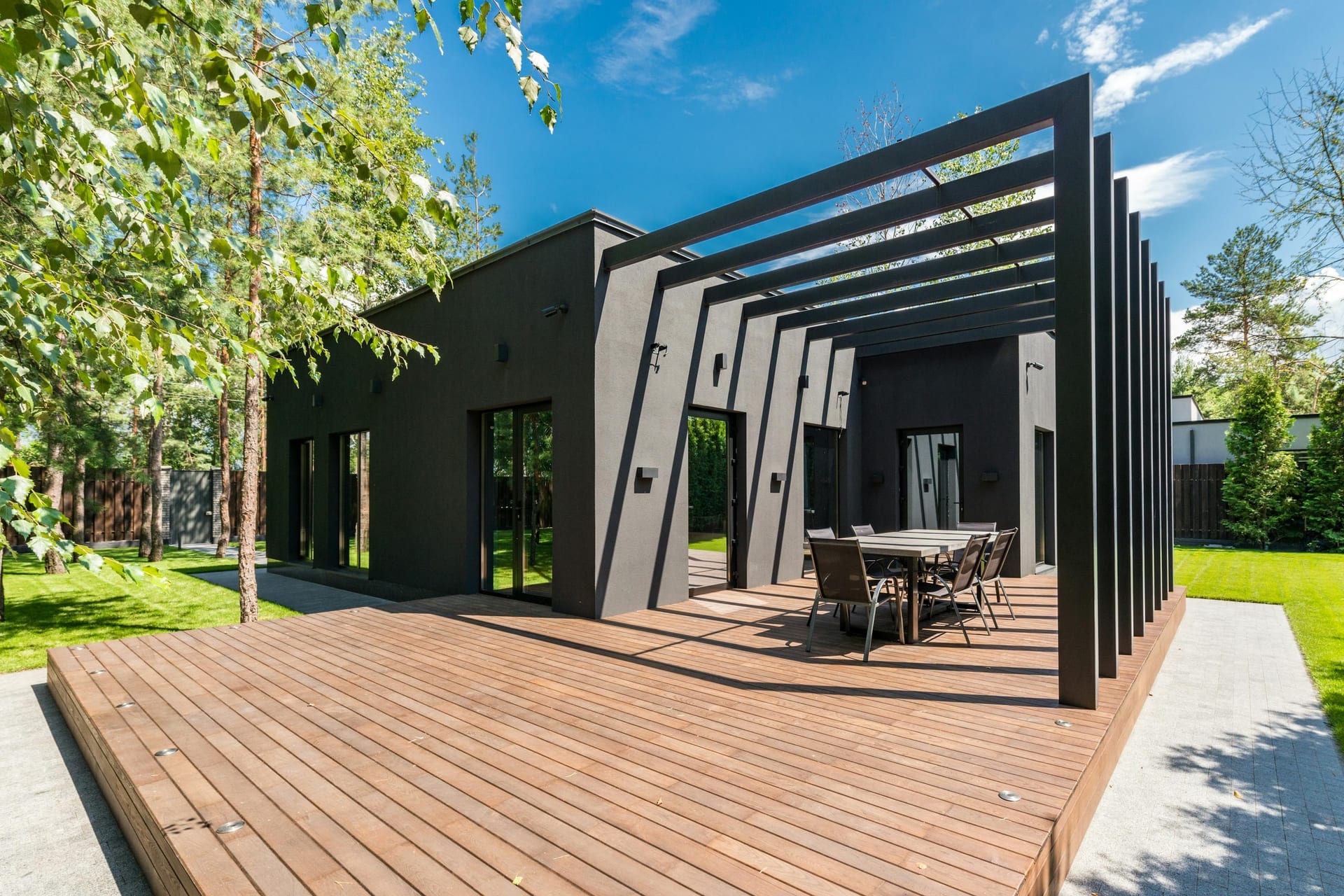A wooden deck with an outdoor dining set surrounded by lush green landscaping