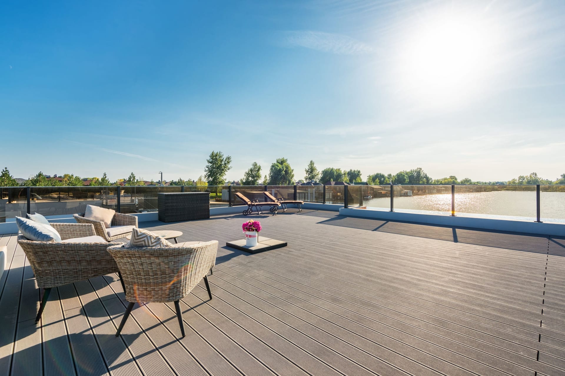 A spacious wood deck with rattan lounge furniture and a cushioned seating area in bright sun