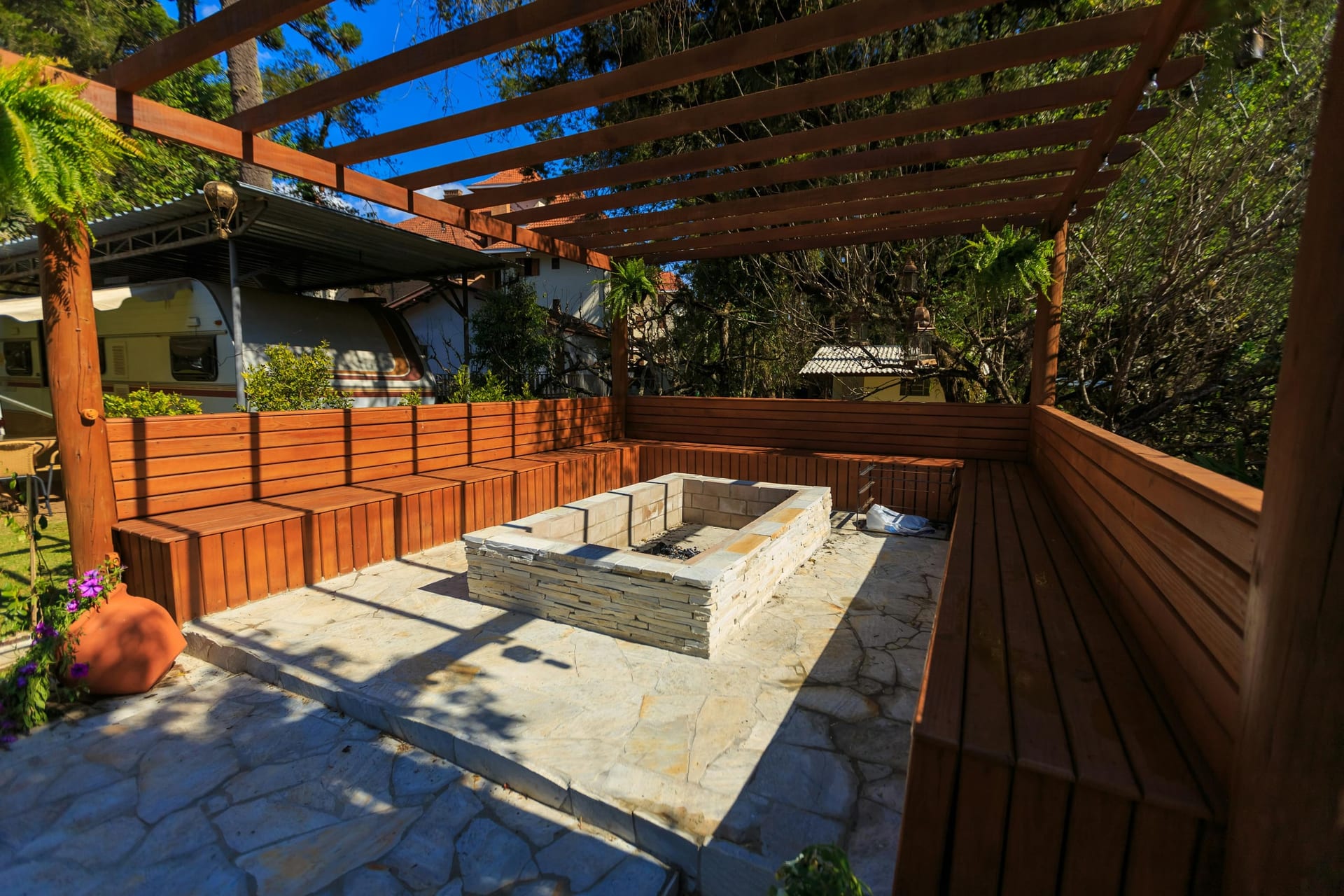 An outdoor patio with a stone fire pit and built-in bench seating under a wood pergola