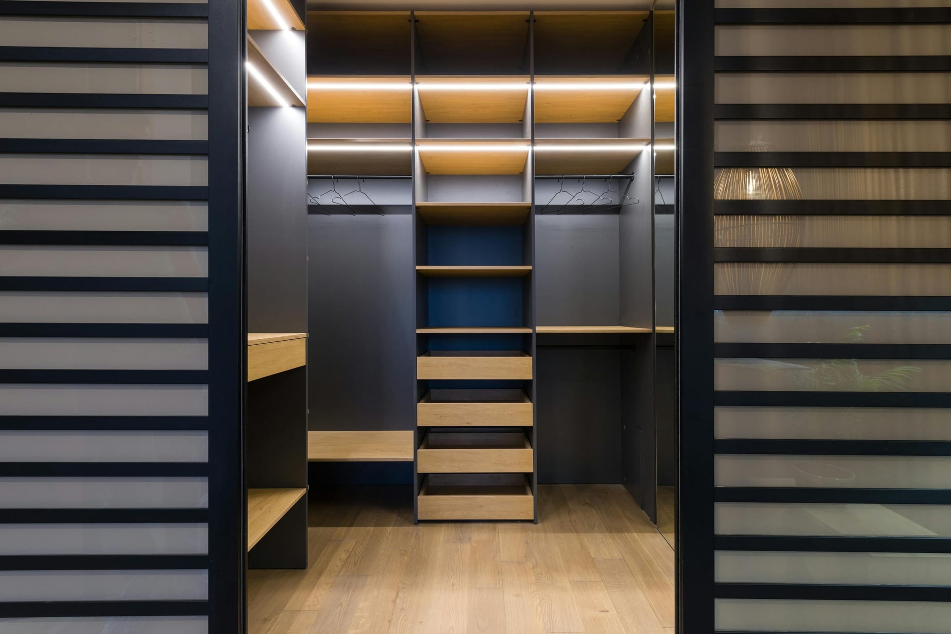 A custom walk-in closet with built-in wood shelving, an island, and accent lighting