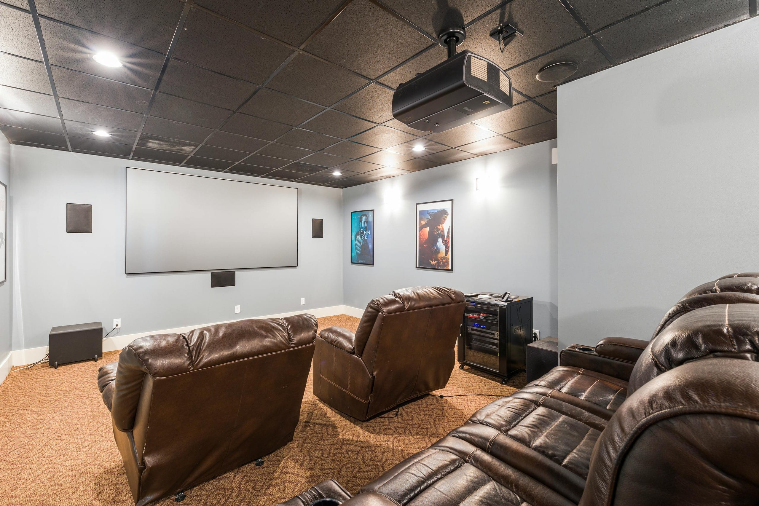 A finished home theater room with tiered leather recliner seating and a large screen