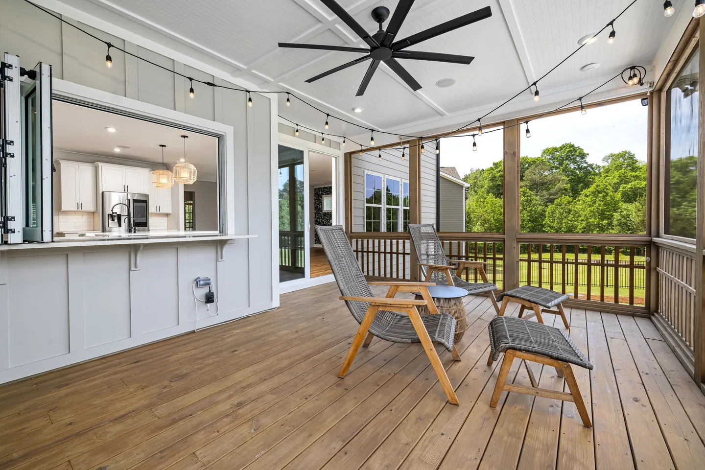 Screened porch with wood decking, lounge chairs, a ceiling fan, and an open kitchen pass-through