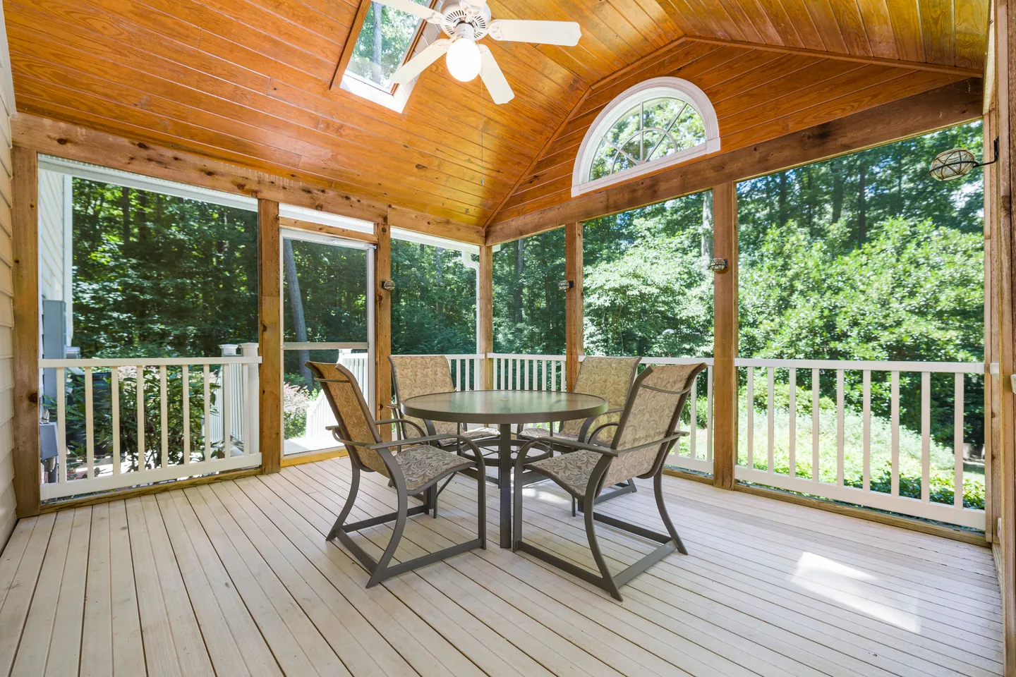 Covered porch with a vaulted timber ceiling, dining table, and screened views of trees