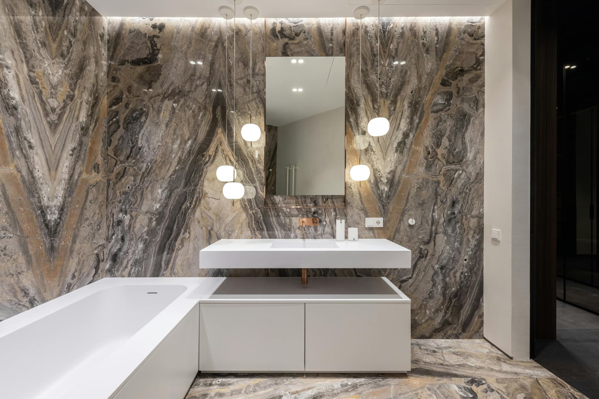 Primary bath with book-matched stone walls, a built-in tub and floating vanity