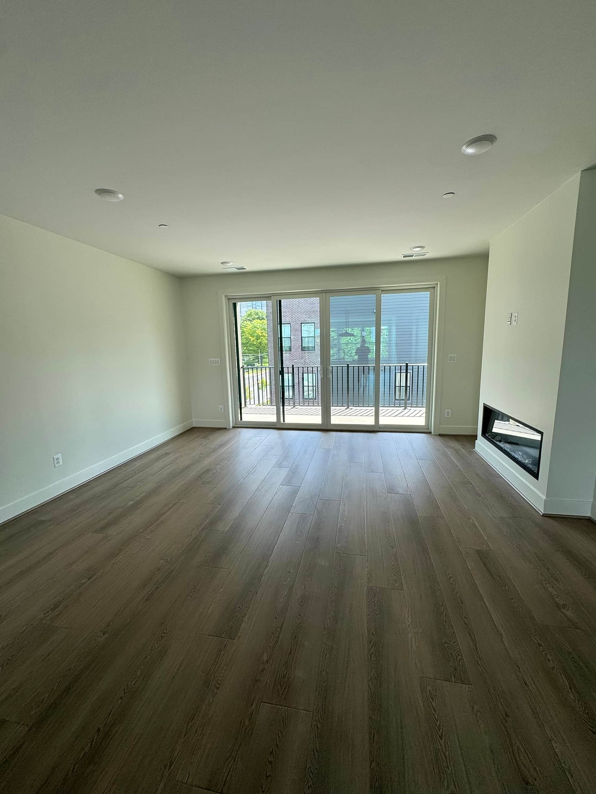 Open living room with wide-plank luxury vinyl plank flooring, a linear fireplace, and sliding doors to the balcony